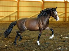 a toy horse is running in an indoor arena with dirt flooring and wooden fences