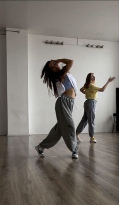 two young women are dancing in an empty room with wood flooring and white walls