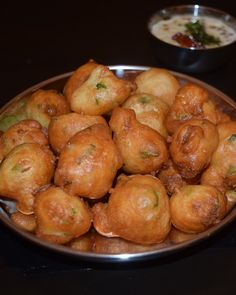 some food that is in a metal bowl on a black table and two bowls with sauces behind it