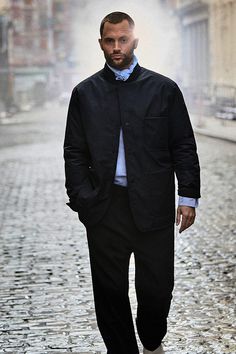 a man walking down a cobblestone street wearing a black jacket and white shirt