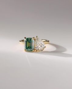 an emerald and diamond ring with two pear shaped diamonds on the side, set in yellow gold