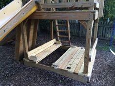 a wooden swing set with a slide in the back ground and some wood slats