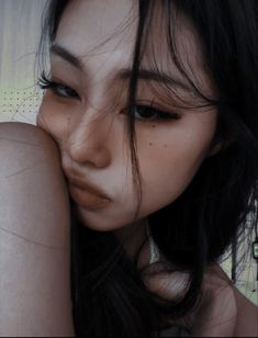 a close up of a person with long black hair and brown eyes holding her hand to her face