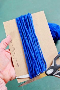 a person holding scissors and yarn in front of a piece of brown paper with blue thread on it