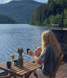 a woman sitting at a wooden table next to a lake