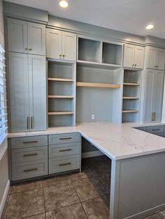 an empty kitchen with gray cabinets and marble counter tops