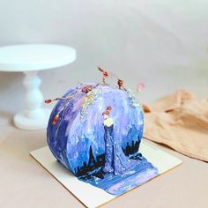 an artistically painted cake sitting on top of a white table next to a plate