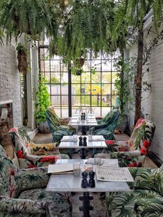 a living room filled with lots of furniture and plants hanging from the ceiling above it