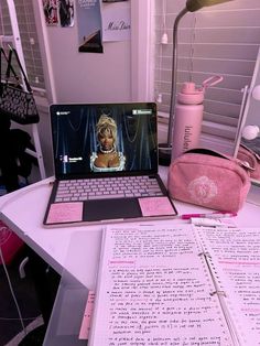 an open laptop computer sitting on top of a desk next to a pink purse and notebook