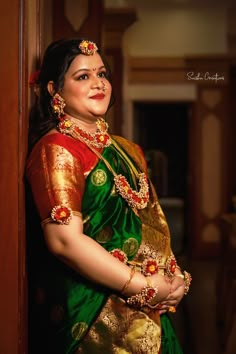 a woman in a green and gold sari posing for the camera with her hands on her hips