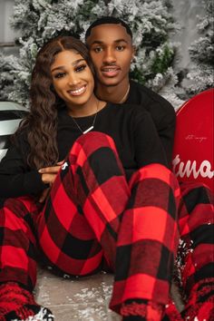 a man and woman sitting next to each other in front of a christmas tree