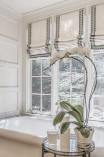 a bath tub sitting next to a window filled with white flowers and greenery on top of a glass table