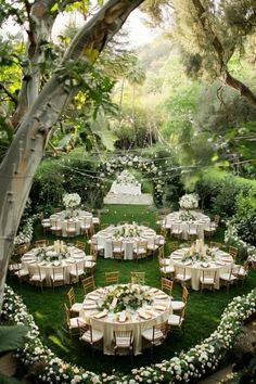 an outdoor wedding reception setup with white flowers and greenery on the lawn, surrounded by trees