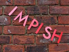 the word impish hanging on a brick wall