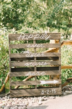 a wooden sign sitting on top of a gravel covered ground next to trees and bushes