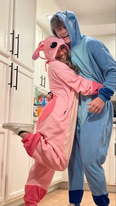 two people dressed in pink and blue onesuits are posing for a photo together