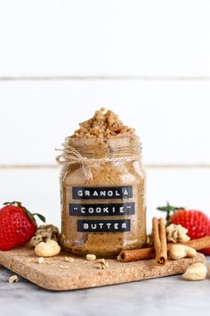 a glass jar filled with granola cookie butter next to cinnamons and strawberries