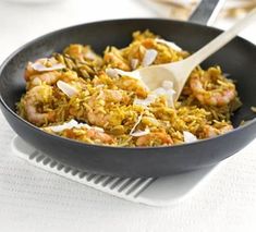 a pan filled with rice and shrimp on top of a white table cloth next to a wooden spoon