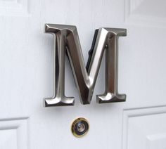 the letter m is made up of metal letters on a white door with a gold knob