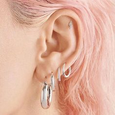 a woman with pink hair is wearing two silver hoop earrings on her left ear and the other half of her right ear