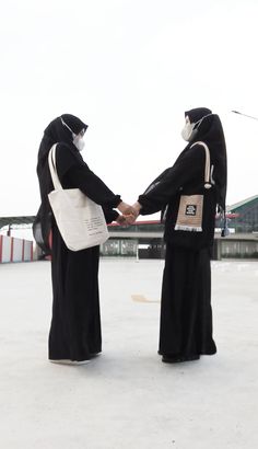 two people dressed in black and white shaking hands with each other while wearing masks on their heads