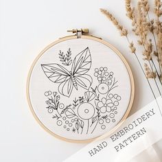 a hand embroidery pattern with flowers and leaves on the hoop next to some dried grass