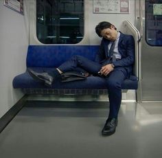 a man in a suit sitting on a subway bench with his head resting on his hand