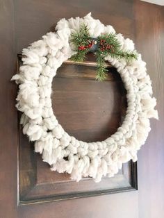 a white yarn wreath hanging on a wooden door with holly berries and red berries in the center