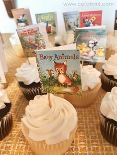 cupcakes with white frosting and brown icing are on a table in front of children's books