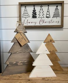 three wooden christmas trees sitting on top of a table next to a sign that says merry christmas