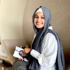 a woman in a hijab smiles while sitting on a chair with a book