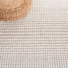 a straw hat sitting on top of a white and beige rug next to a basket