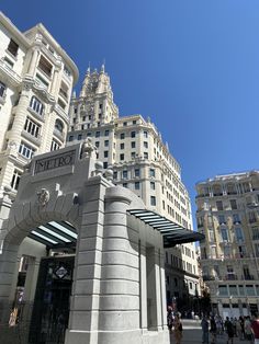 people are walking around in front of tall buildings on a sunny day with blue skies