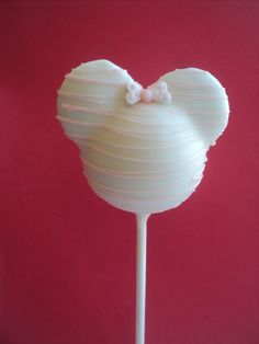 a white mickey mouse lollipop with a bow on it's head, against a red background