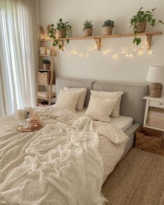 a bed with white sheets and pillows in a bedroom next to a window filled with potted plants