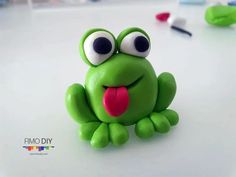 a green toy frog sitting on top of a white table with its tongue sticking out