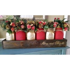 four red mason jars with pine cones and greenery in them on a blue dresser