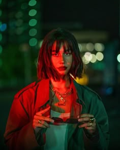 a woman with red hair and piercings holding a cell phone in her hands at night