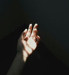 a person's hand reaching up towards the light coming in from behind them on a black surface