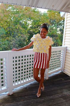 a woman standing on a porch wearing a red and white striped dress with ruffles