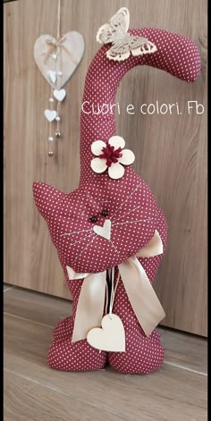 a red and white stuffed animal sitting on top of a wooden floor next to a wall