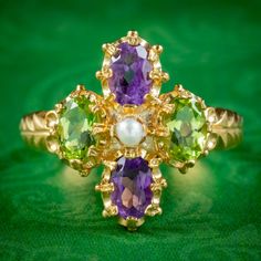 A striking Suffragette style ring claw set with two violet amethysts, two green peridots (approx. 0.45ct each) and a central white pearl. Together, the colours of each stone pay tribute to the women's Suffragette movement and symbolise; Violet for Loyalty, White for Purity and Green for Hope, or Give Women Votes!  The ring is fashioned in gold gilded silver and displays beautiful engraving across the gallery and shoulders. It boasts a colourful collection of gemstones and looks lovely crowning t Green Amethyst Rings In Fine Jewelry Style, Green Amethyst Ring With Oval Shape For Weddings, Green Oval Amethyst Ring For Wedding, Green Amethyst Birthstone Ring In Fine Jewelry Style, Green Amethyst Birthstone Ring, Green Amethyst Ring Fine Jewelry, Green Multi-stone Amethyst Ring, Green Multi-stone Amethyst Wedding Ring, Green Amethyst Ring For Anniversary, May Birthstone