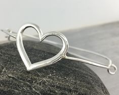 "This listing for 1 Sterling Silver Heart Adjustable Bangle Bracelet This solid sterling silver bracelet features a 1-inch heart that is the centerpiece of an adjustable style bangle. The bangle itself is made of Sterling Silver, then plated in Rhodium to prevent tarnish. Everything in my shop is handmade in my studio, please allow 3-5 business days before we ship :) The bangle can be adjusted to both slide the bangle over the knuckles and to tighten/loosen the fit of the bangle. The bracelet is Sterling Silver Open Heart Bracelet For Mother's Day, Adjustable Heart Shaped Sterling Silver Bracelet For Valentine's Day, Silver Heart Charm Bangle Bracelet, Adjustable Open Heart Bracelets For Anniversary, Silver Open Heart Bracelet For Gift, Silver Open Heart Bracelet As Gift, Silver Open Heart Bracelet For Valentine's Day, Heart-shaped Sterling Silver Bracelet For Weddings, Silver Open Heart Bracelet For Mother's Day