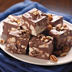 a white plate topped with pieces of chocolate covered in nuts and caramels next to a blue napkin