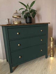 a dark green dresser with gold handles and brass knobs, next to a potted plant