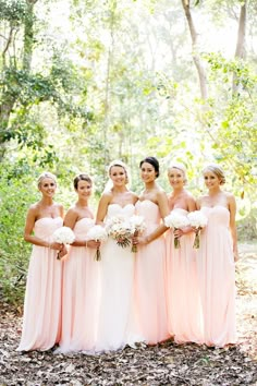 a group of women standing next to each other wearing pink dresses and holding bouquets