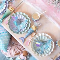 a table topped with plates and cups filled with mermaid themed food next to other items