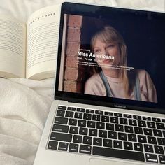 an open laptop computer sitting on top of a white bed next to an open book