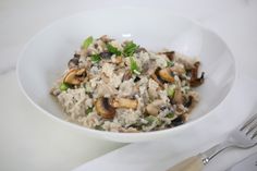 a white bowl filled with rice and mushrooms next to a silver fork on top of a table