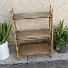 two wooden shelves sitting next to each other on the side of a building with potted plants